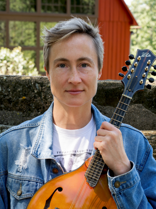 Gabriel Jenks, a composer in a denim shirt with short hair, holds a mandolin